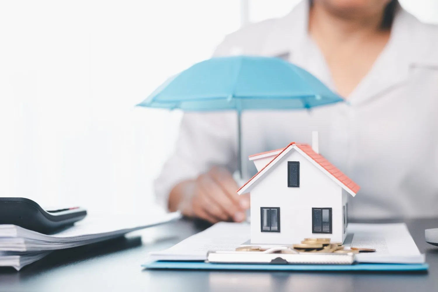 A model house sheltered under a small blue umbrella on a desk