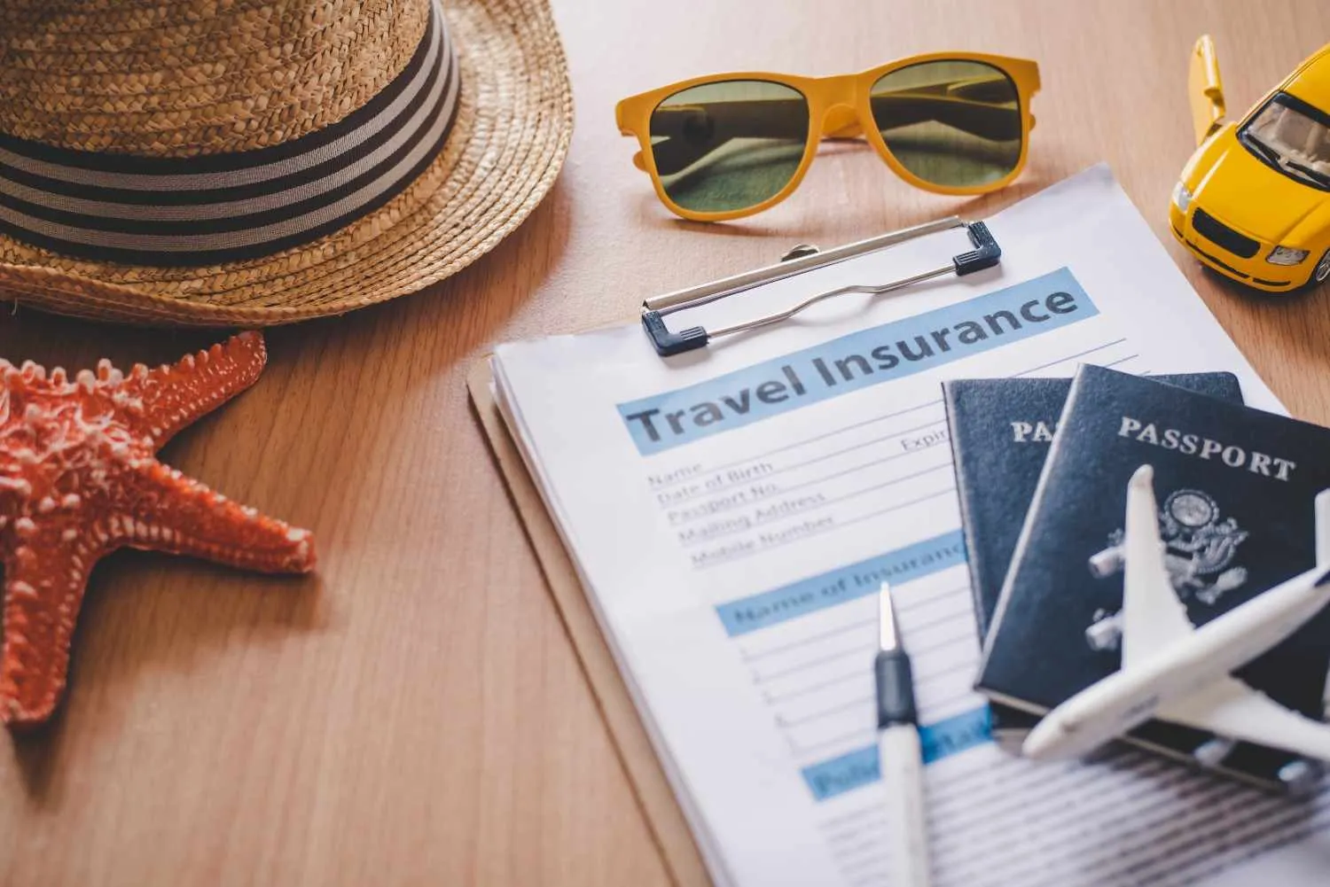 A travel insurance form with passports, a sun hat and sunglasses
